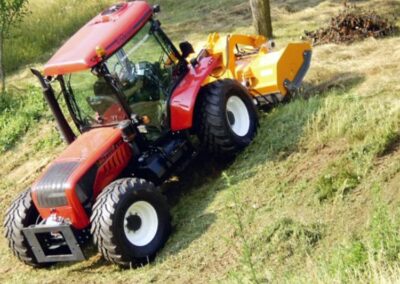 A red tractor mowing grass on a hillside.